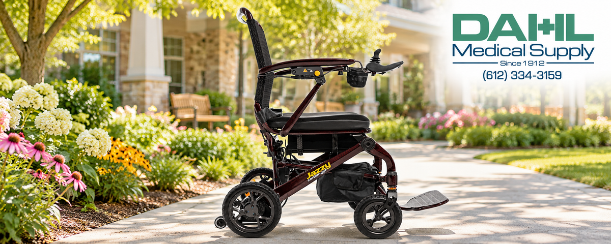 Black Cherry Pride Jazzy Carbon 27 power wheelchair on a paved garden path outside a senior living community, with flowers and the Dahl Medical Supply logo in the upper-right corner.