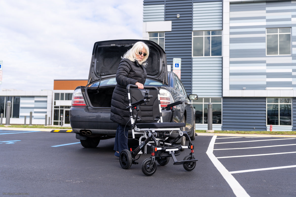 User lifting the Pride Jazzy Carbon from a car trunk for transport.