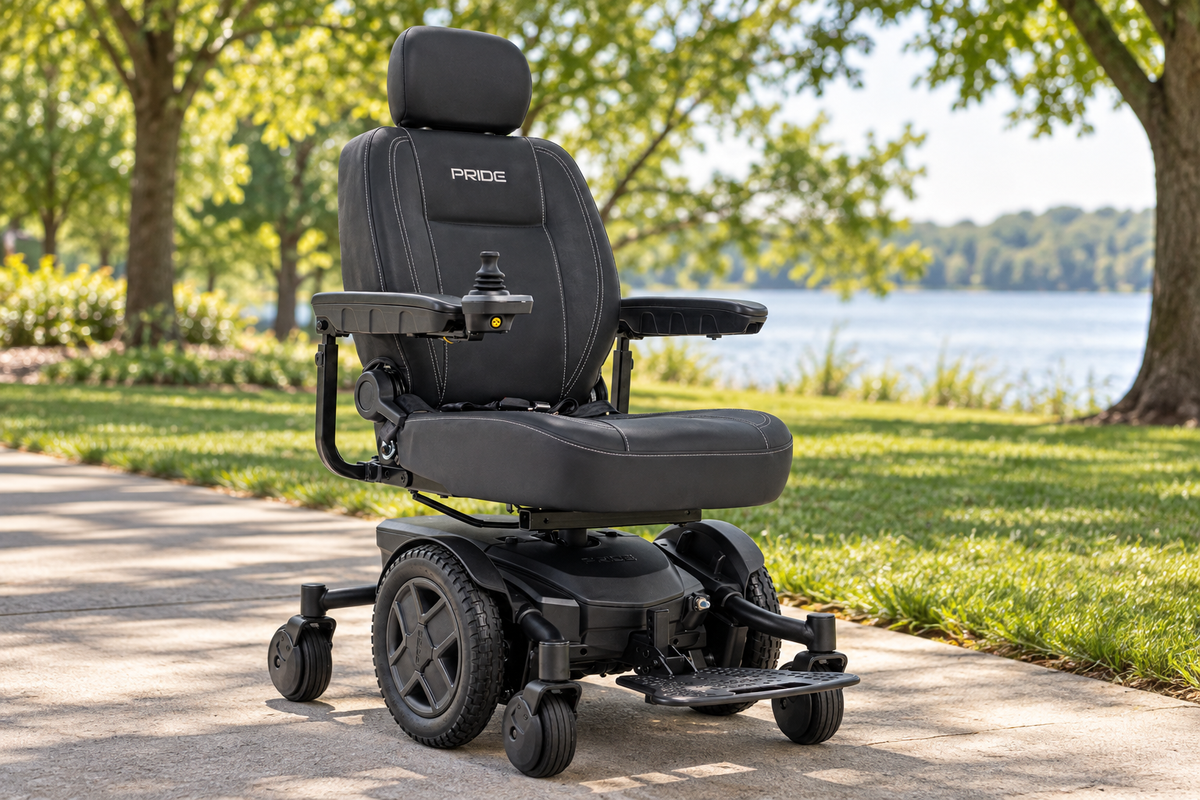 Black Pride Jazzy EVO powerchair on a paved lakeside park path, with padded seating, a headrest, joystick, and footplate beneath sunlit trees.