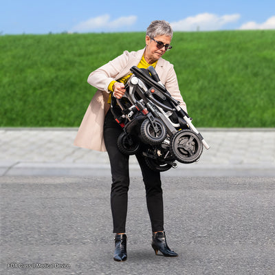 User carrying the folded Pride Jazzy Carbon power wheelchair with ease.