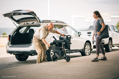 User carrying the folded Pride Jazzy Carbon near an airport vehicle.
