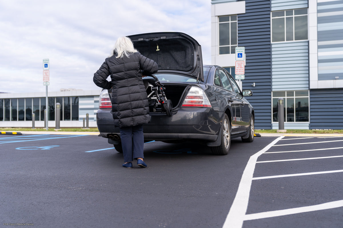 User placing the folded Pride Jazzy Carbon into a vehicle trunk.