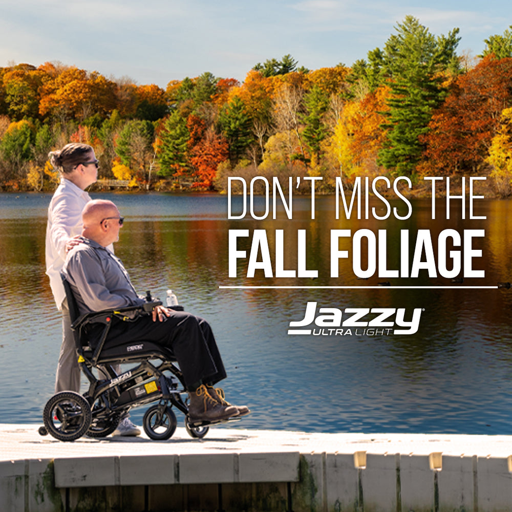 Man driving a Jazzy Ultra Light with women next to him on a dock looking over a lake with fall color trees in the background.
