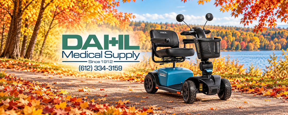 Iceberg Blue Pride Victory Platinum 4-wheel mobility scooter on a lakeside path surrounded by fall foliage, with the Dahl Medical Supply logo to the left.